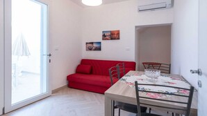 A room with a red sofa, a dining table with chairs, a hanging light fixture, and an air conditioning unit. - Lovely apartment in villa for 4 people with A/C, TV and patio (Salve)