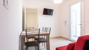 A dining area with a wooden table and four chairs, a flat-screen TV mounted on the wall, and a red sofa in the foreground. - Lovely apartment in villa for 4 people with A/C, TV and patio (Salve)