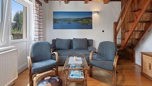 Un salon chaleureux avec un canapé, deux fauteuils, une table basse et un escalier en bois.