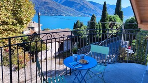 A balcony with a table and chairs, overlooking a lake and mountains.