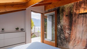 A bedroom with a large bed, a wooden ceiling, a sliding glass door leading to a balcony, and a wall with a textured mural.