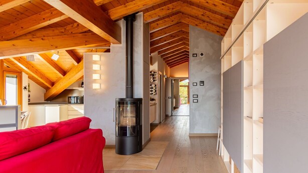 A modern interior with a wooden ceiling, a central fireplace, a red sofa, and a kitchen area.