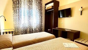 A hotel room with two beds, a TV mounted on the wall, a wardrobe, and a desk.