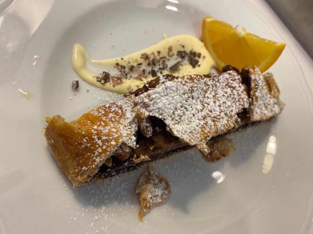 A dessert with powdered sugar, a slice of orange, and a dollop of cream on a white plate.