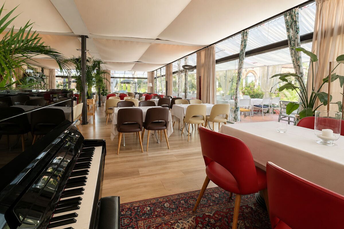 Un espace repas comprenant des tables, des chaises, un piano et de grandes fenêtres.