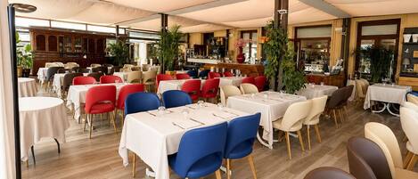 Un restaurant avec plusieurs tables et chaises, un coin bar et un buffet en bois à l’arrière-plan.