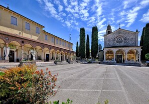 A courtyard with a building featuring arched windows and a bell tower, surrounded by neatly trimmed hedges. - Locanda al Santuario (Peschiera del Garda)