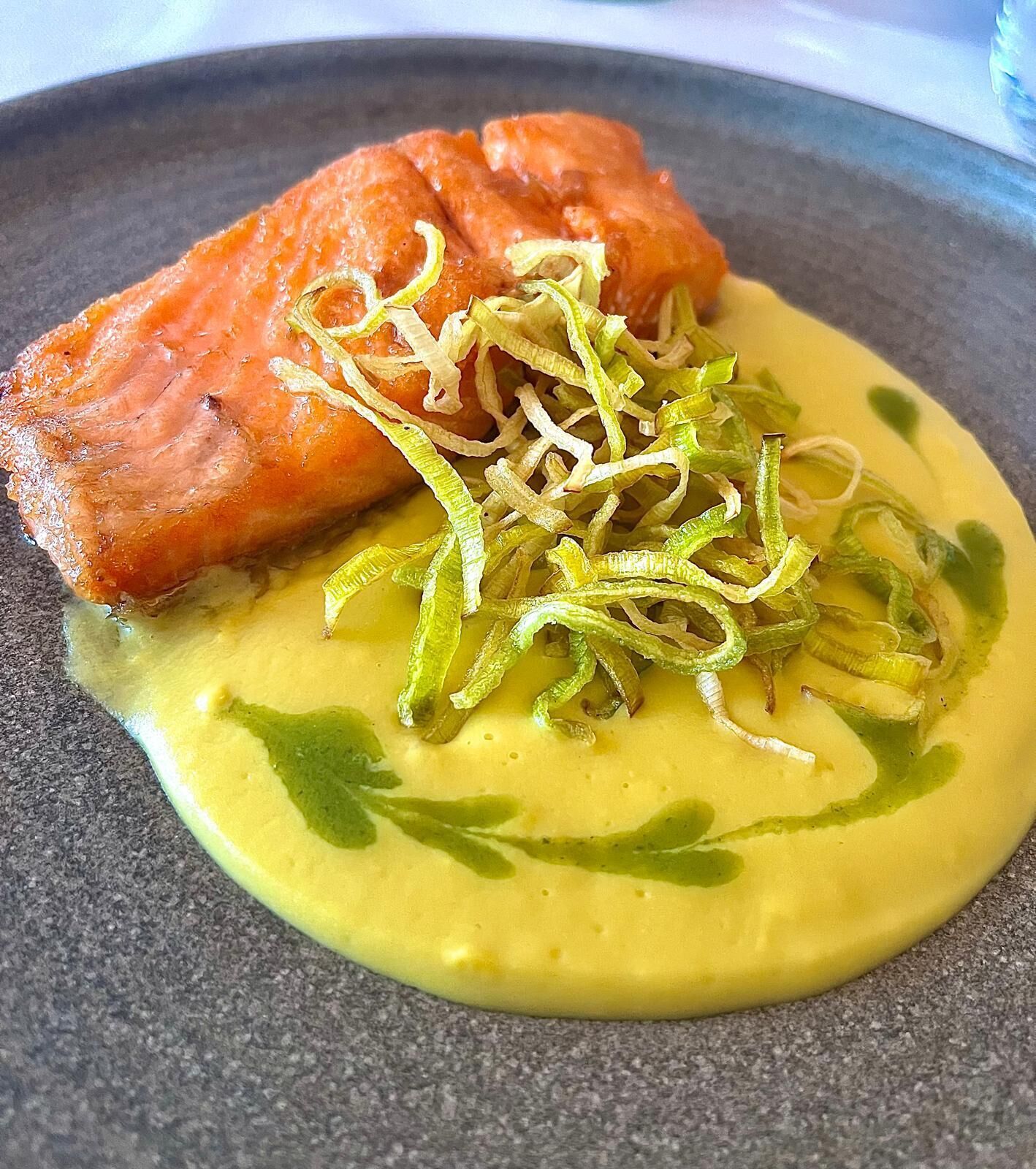 Ein Teller mit Lachs, grüner Beilage und gelber Soße.