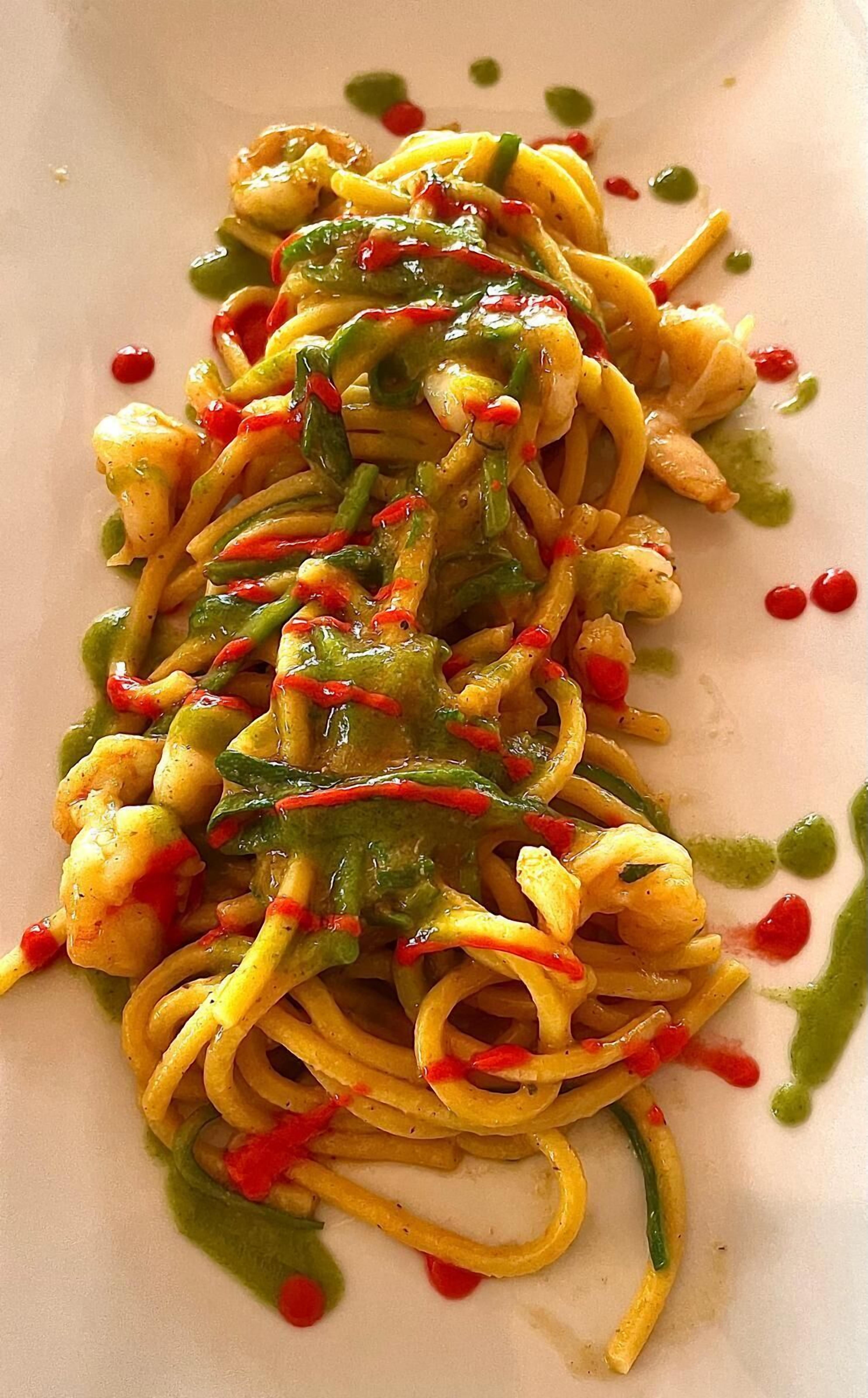A plate of spaghetti with green sauce and red pepper flakes.