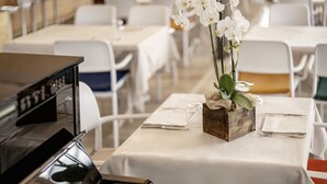 A dining area with white tables, a piano, and a floral centerpiece. - Locanda al Santuario (Peschiera del Garda)