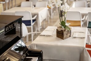 A dining area with white tables, a piano, and a floral centerpiece. - Locanda al Santuario (Peschiera del Garda)