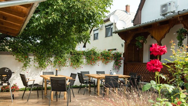 An outdoor patio with a wooden table and chairs, surrounded by greenery and flowers. - Nice apartment for 10 people with private pool, WIFI, A/C, TV and balcony (Marcali)
