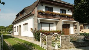 A two-story house with a sloped roof, a balcony with red flowers, and a gated entrance. - Nice apartment for 10 people with private pool, WIFI, A/C, TV and balcony (Marcali)