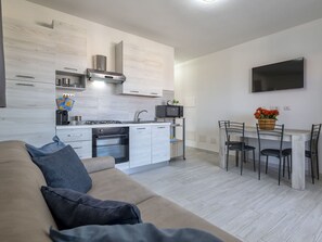 A modern kitchen with a built-in oven and microwave, a dining area with a table and chairs, and a flat-screen TV mounted on the wall.