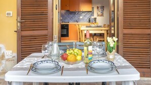 Une table de jardin dressée pour un repas en plein air, avec des assiettes, des couverts, une bouteille de vin, des verres et un saladier de fruits.