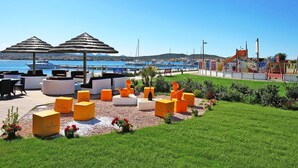 A coastal outdoor seating area with umbrellas, a children's play area, and a marina in the background. - Beautiful apartment for 5 people with A/C, TV and terrace (Regia Dogana)