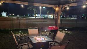 An outdoor patio area with a fire pit table and four chairs, surrounded by a wooden fence and a covered seating area. - Luxurious 37' 5th Wheel. Enjoy all the fun of Glamping  (Forks)