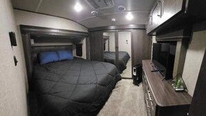 A compact RV bedroom with two beds, a small TV, and a kitchenette area. - Luxurious 37' 5th Wheel. Enjoy all the fun of Glamping  (Forks)