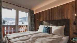 Ein Schlafzimmer mit einem großen Bett, Holzwandverkleidungen, einem Balkon mit Blick auf verschneite Berge und einem Hollerker.