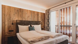 A bedroom with a wooden headboard, a bed with white linens, a bedside table, and a view of a wooden balcony. - Lovely apartment for 6 guests with WIFI, TV, balcony and panoramic view (Dienten Am Hochkönig)