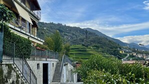 A multi-story building with a staircase leading to an entrance, surrounded by greenery and a mountainous backdrop. - Lovely apartment for 4 people with WIFI, TV, balcony and pets allowed (Vendrogno)