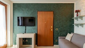 A modern living room with a wooden door, a television mounted on the wall, a small table, and a sofa. - Lovely apartment for 4 people with WIFI, TV, balcony and pets allowed (Vendrogno)
