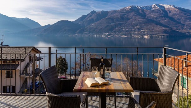 A terrace with wicker furniture, a wooden table, and a view of a lake and mountains. - Lovely apartment for 4 people with WIFI, TV, balcony and pets allowed (Vendrogno)