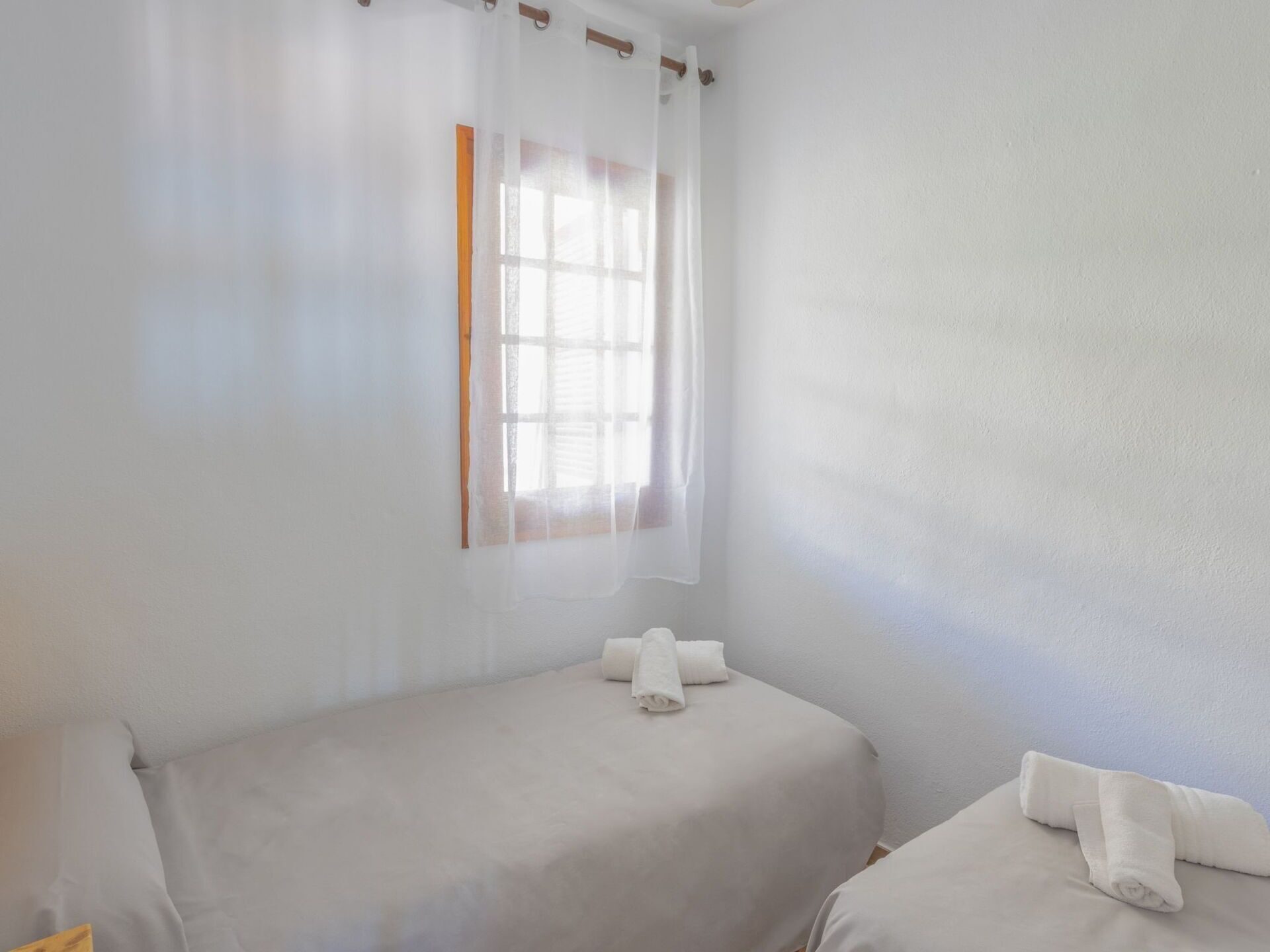Ein Zimmer mit zwei Betten, einem Fenster mit durchsichtigem Vorhang und einem Handtuch auf jedem Bett.