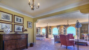 A spacious living area with a wooden cabinet, a red patterned rug, and a chandelier. There are framed pictures on the wall and a view of an outdoor patio with a dining area. - Beautiful private villa with WIFI, private pool, A/C, TV, patio, pets allowed and panoramic view (Montecatini)