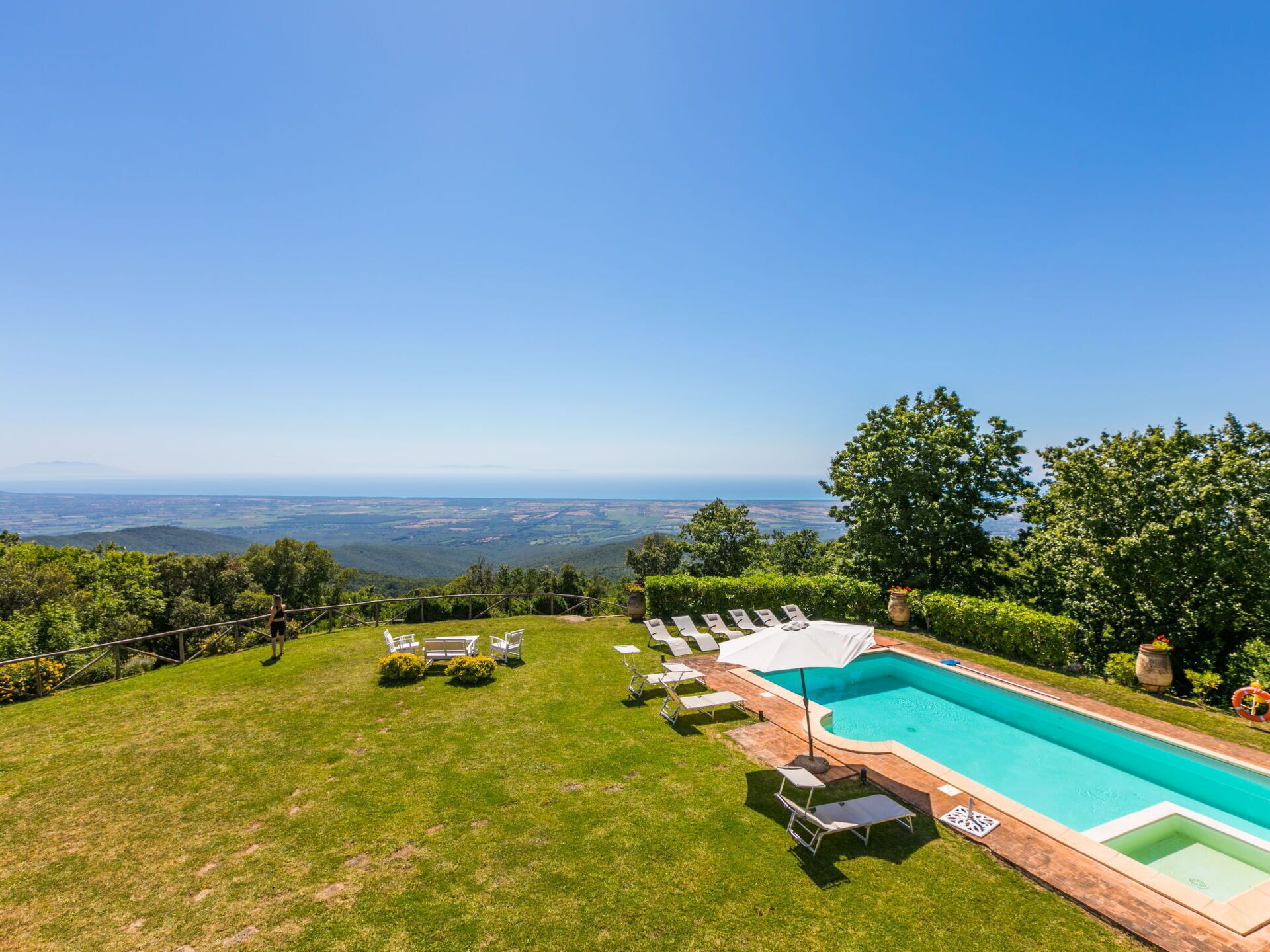 Une piscine entourée de chaises longues et de parasols, elle-même bordée d’une pelouse bien entretenue et d’arbres, le tout offrant une vue panoramique sur le paysage environnant.
