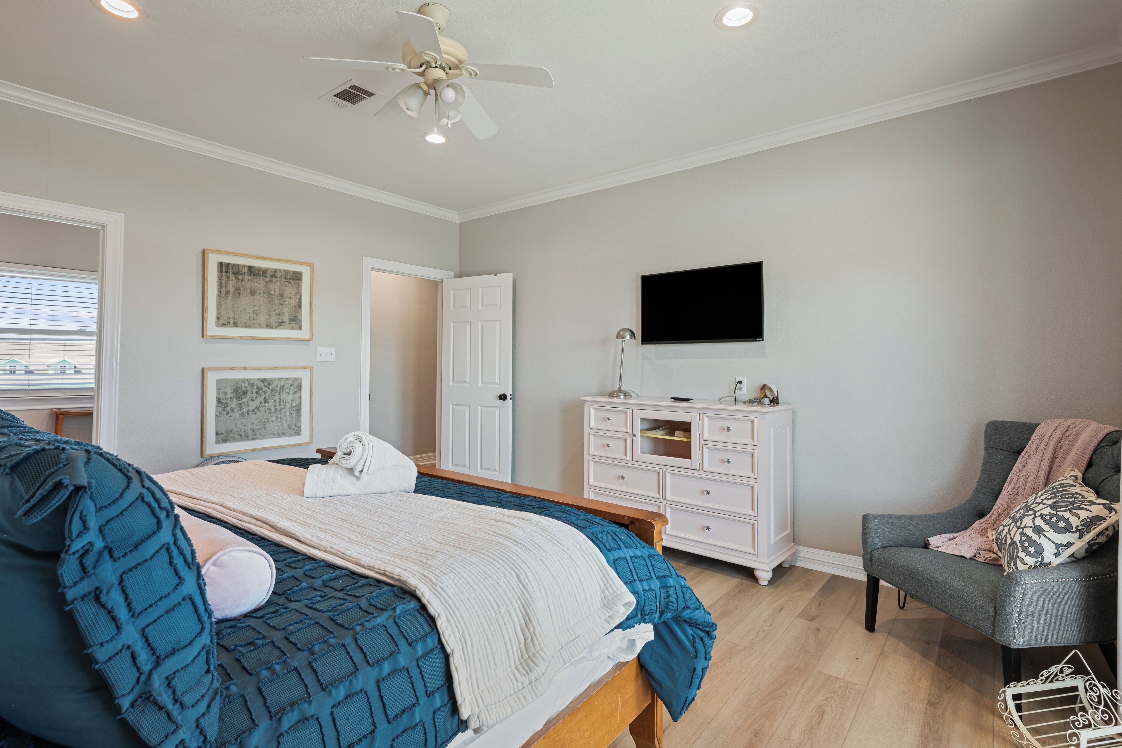 A bedroom with a bed, a dresser, a chair, a ceiling fan, and a television.