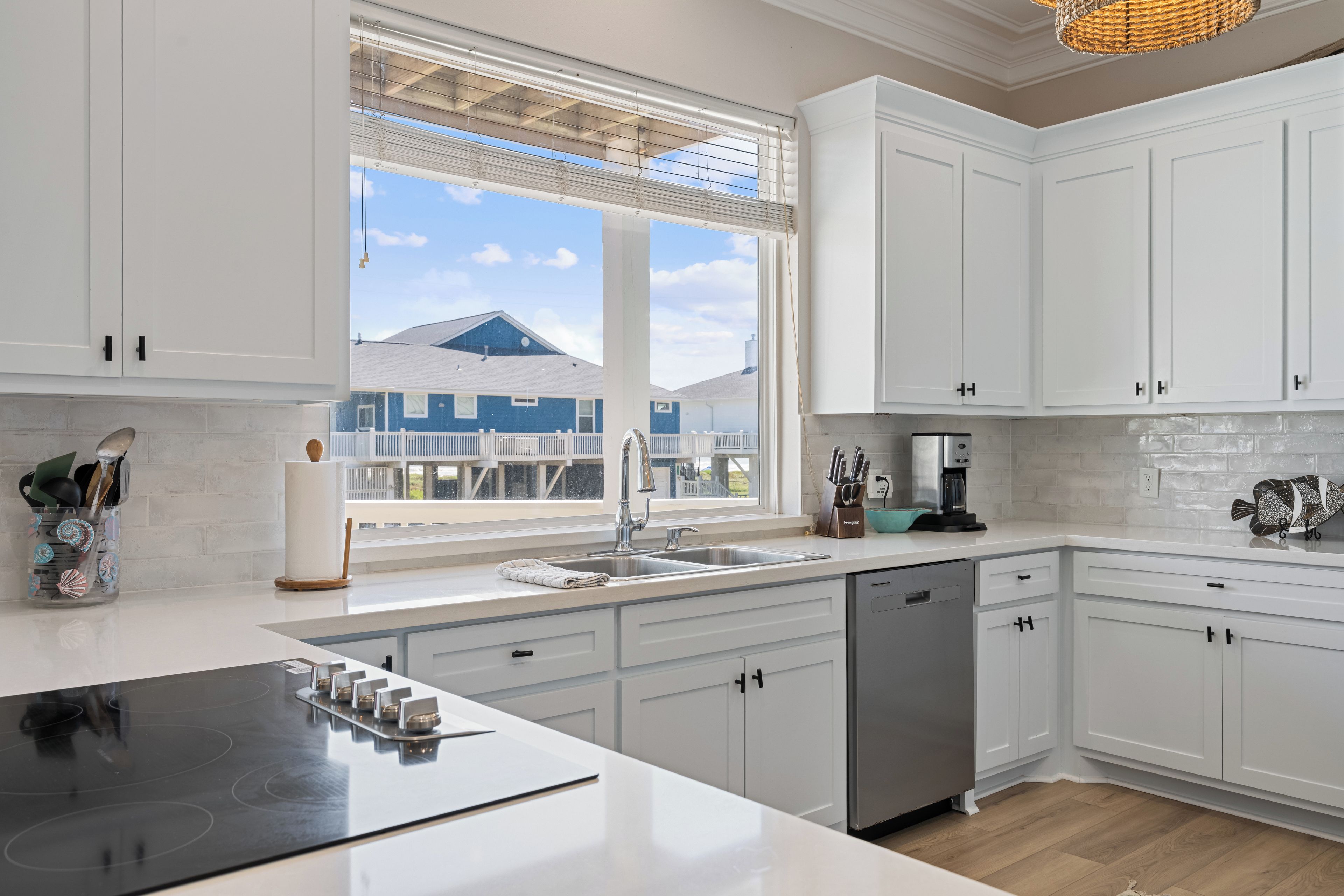A modern kitchen with white cabinetry, a built-in dishwasher, and a large window with blinds.