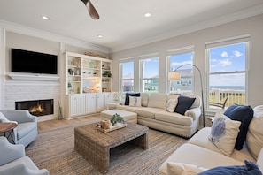 A spacious living room with a fireplace, a television, and a large window offering a view of the ocean. - Unbeatable LOCATION, first row, Oceanfront! (Bolivar Peninsula)