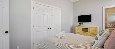 Une chambre à coucher avec un lit, une commode, un téléviseur et une porte.