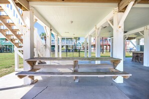 Un espace pique-nique extérieur abrité, avec une table et des bancs en bois, entouré d’une rambarde blanche et offrant une vue sur les bâtiments en arrière-plan.