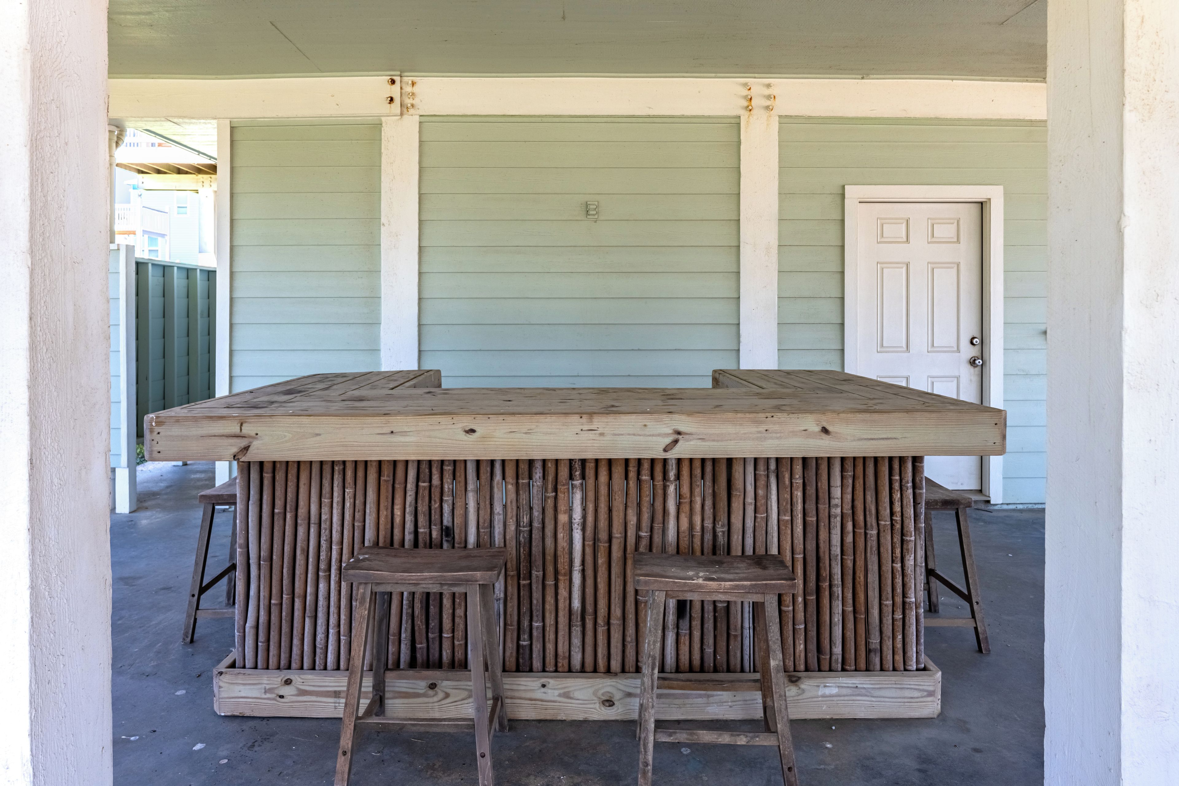 A bar area with a wooden top and stools, set against a green wall with a door.