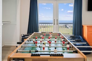 Une table de baby-foot dans une pièce offrant une vue sur la mer grâce à de grandes fenêtres.
