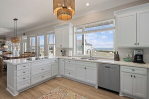 A modern kitchen with white cabinetry, a large island, a built-in dishwasher, and a view of the ocean. - Unbeatable LOCATION, first row, Oceanfront! (Bolivar Peninsula)