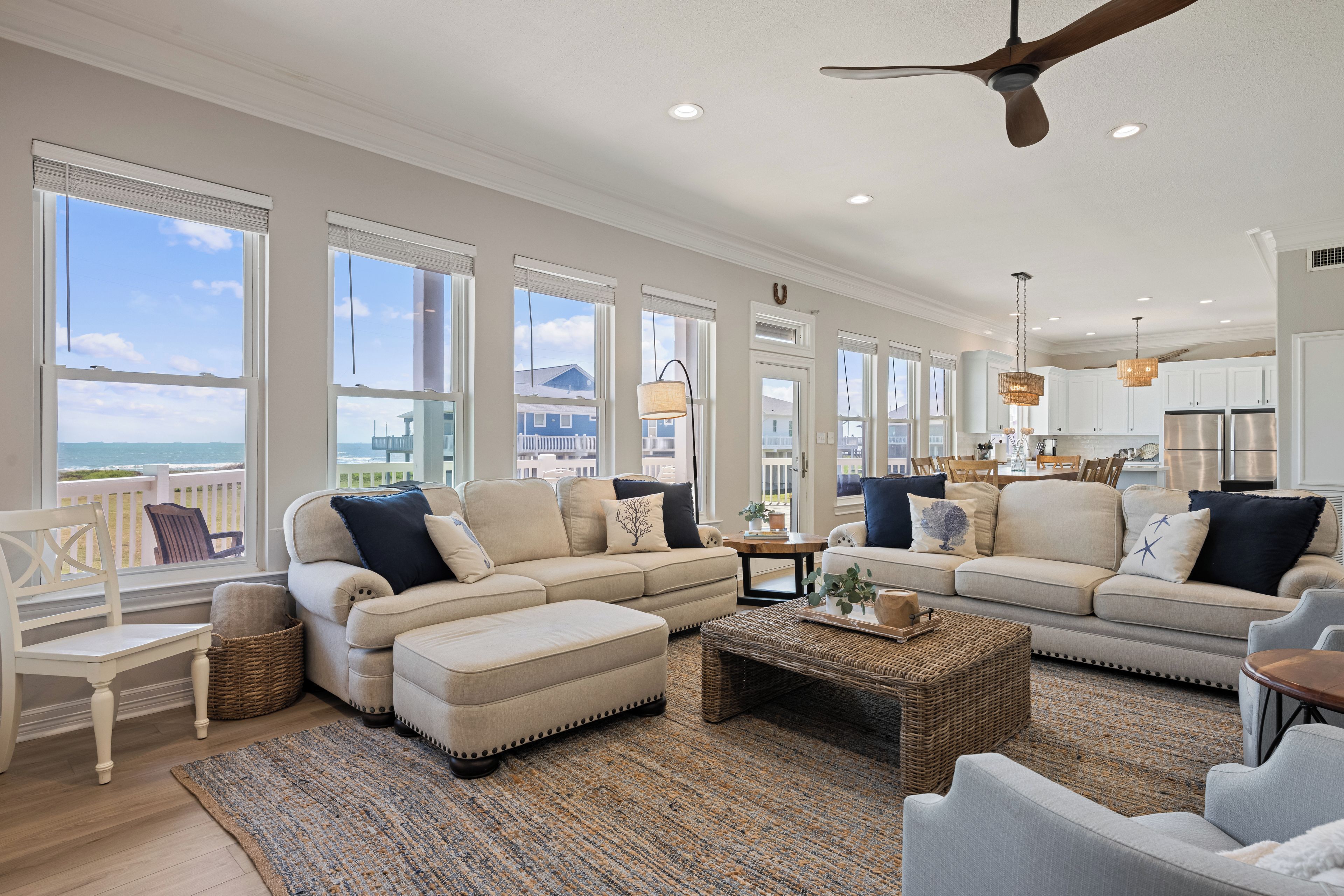 A spacious living room with large windows, a ceiling fan, and a view of the ocean.