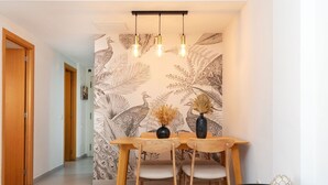 A dining area with a wooden table and chairs, a glass coffee table, and a wall with a peacock and leaf pattern. - Beautiful apartment for 4 people with pool, WIFI, A/C, TV and terrace (Lloret De Mar)