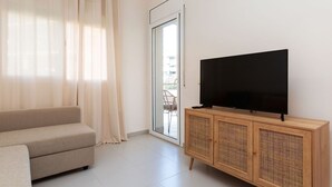 A living room with a sofa, a television on a wooden cabinet, and a sliding glass door leading to an outdoor area. - Beautiful apartment for 4 people with pool, WIFI, A/C, TV and terrace (Lloret De Mar)