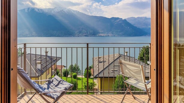 Ein Balkon mit Blick auf einen See und Berge, zwei Liegestühle und ein gefliester Boden.