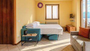 Ein Schlafzimmer mit Bett, einer Couch, einem kleinen Tisch, einem Heizkörper, einem Fenster und Blick ins Freie.