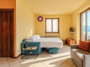Une chambre à coucher comprenant un lit, un canapé, une petite table, un radiateur, une fenêtre et une vue sur l’extérieur.
