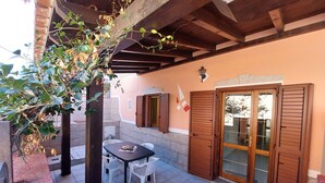 Un patio al aire libre con una mesa, sillas, una puerta de madera y un muro con un emblema decorativo.