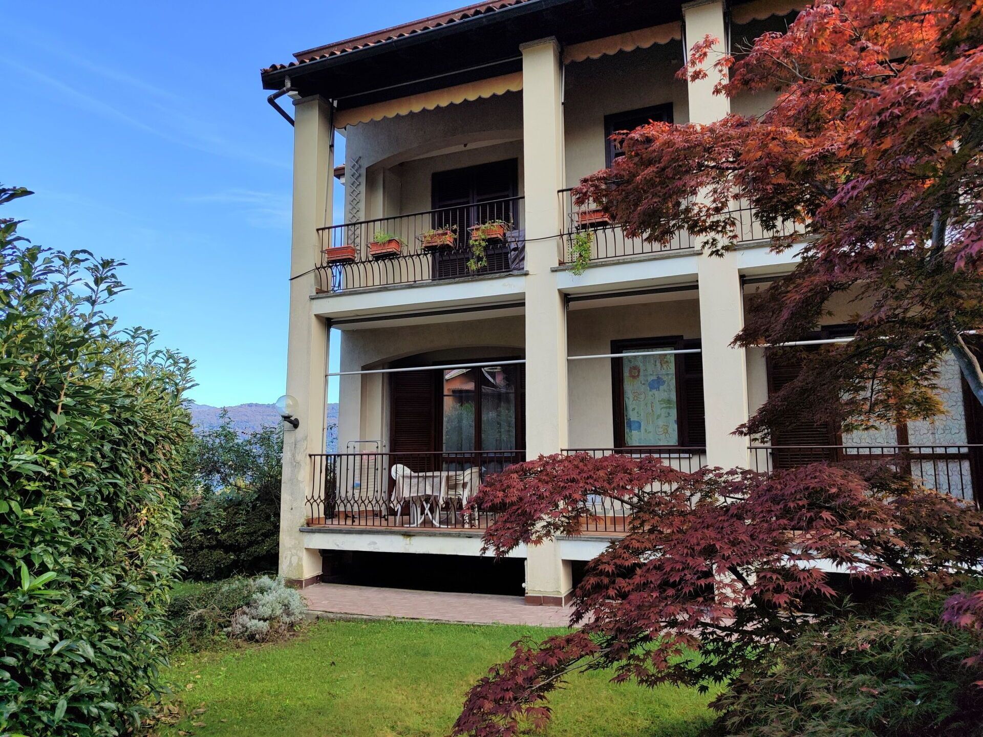 A multi-story building with balconies, a garden, and a view of the mountains.