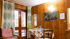 A dining area with wooden walls, a table with a quilted tablecloth, and a chair with a floral pattern.