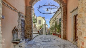 A narrow stone-paved street with an archway, potted plants, and a bell tower. - Cosy apartment for 2 people with WIFI, A/C, balcony and pets allowed (Marciana)