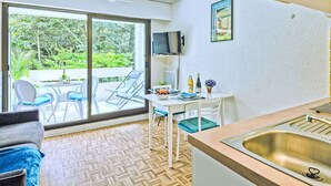 Een compacte keuken met een spoelbak, een eethoek met stoelen, een televisie en uitzicht op groen via de schuifdeur.