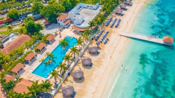 An aerial view of a resort with a swimming pool, beach, and a pier.